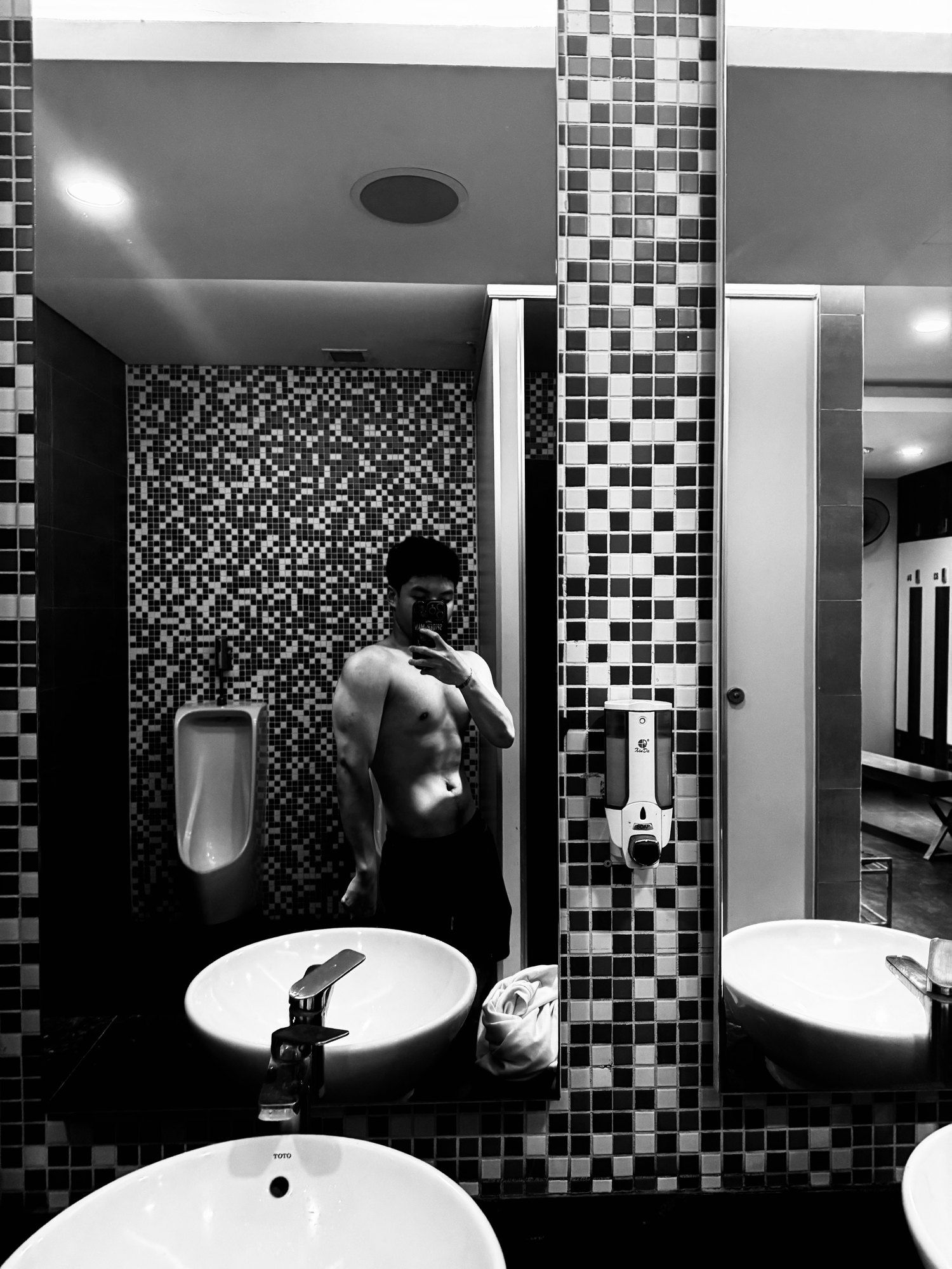 Black-and-white full-length mirror photo in a gym bathroom.