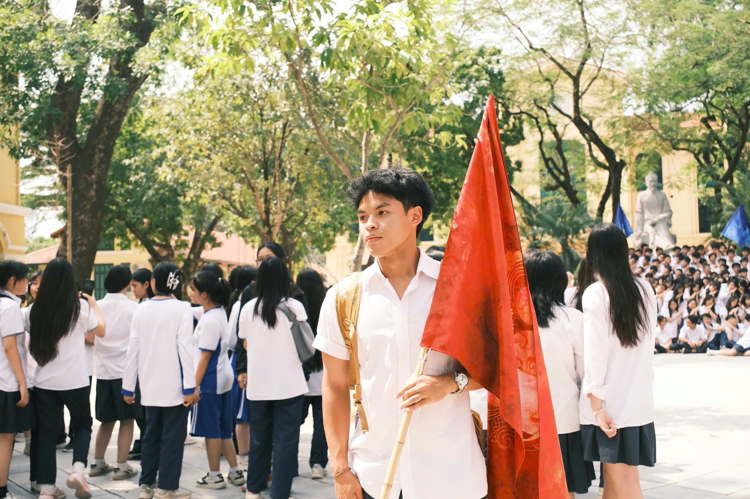 Bao holding a red flag in the schoolyard among students in uniform.