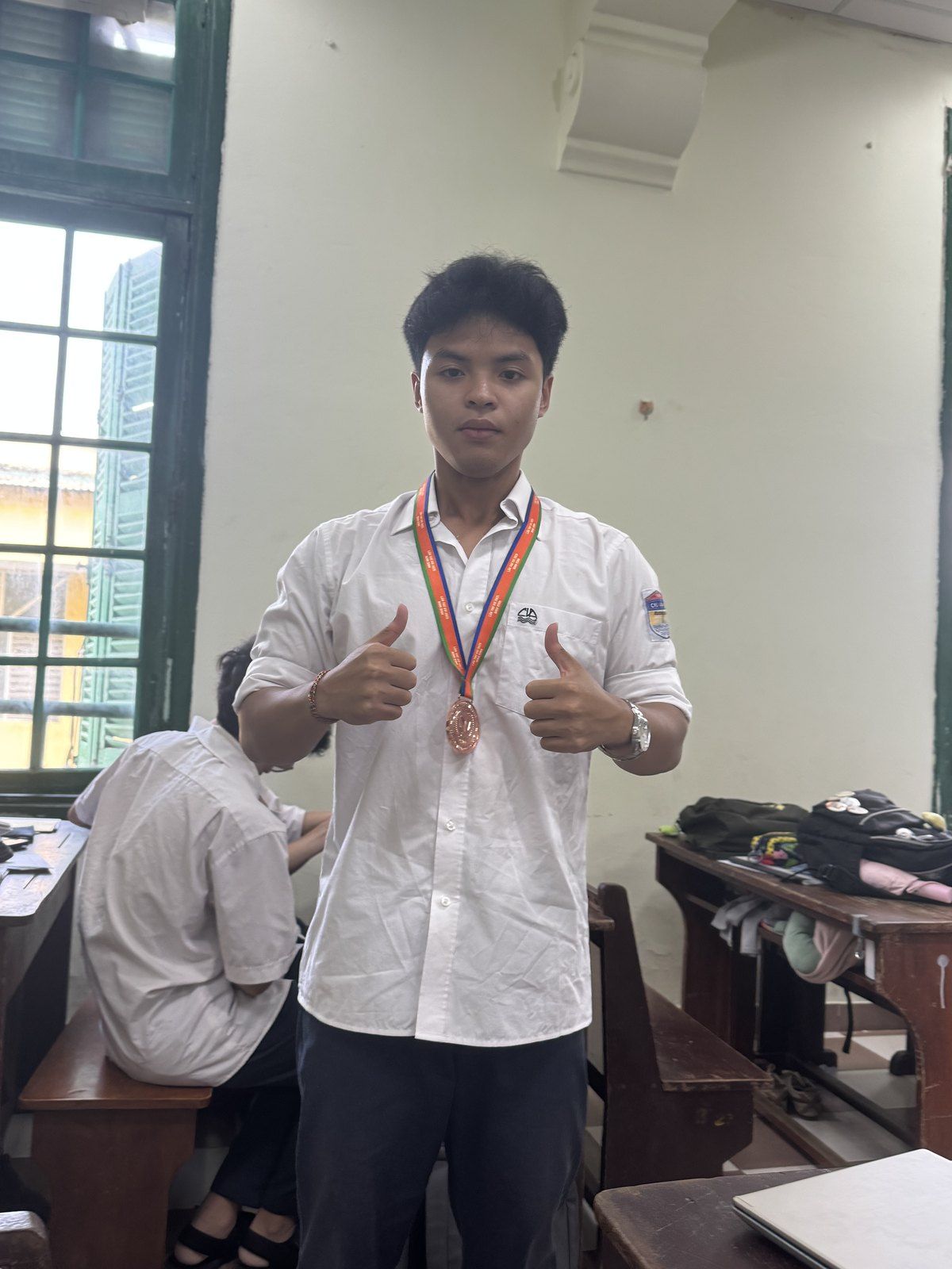 Bao wearing a medal and giving a thumbs up in a classroom.