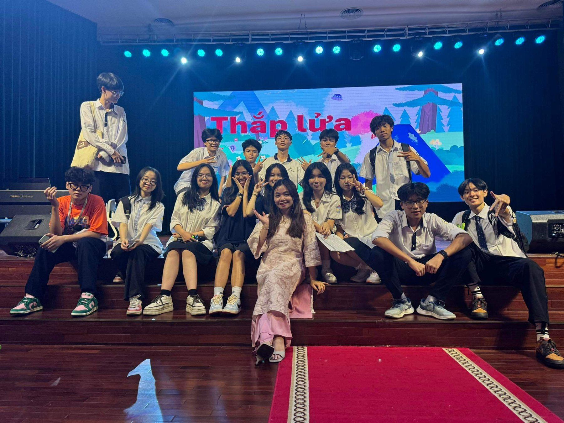 A group of students on stage in front of a “Thắp lửa” screen.