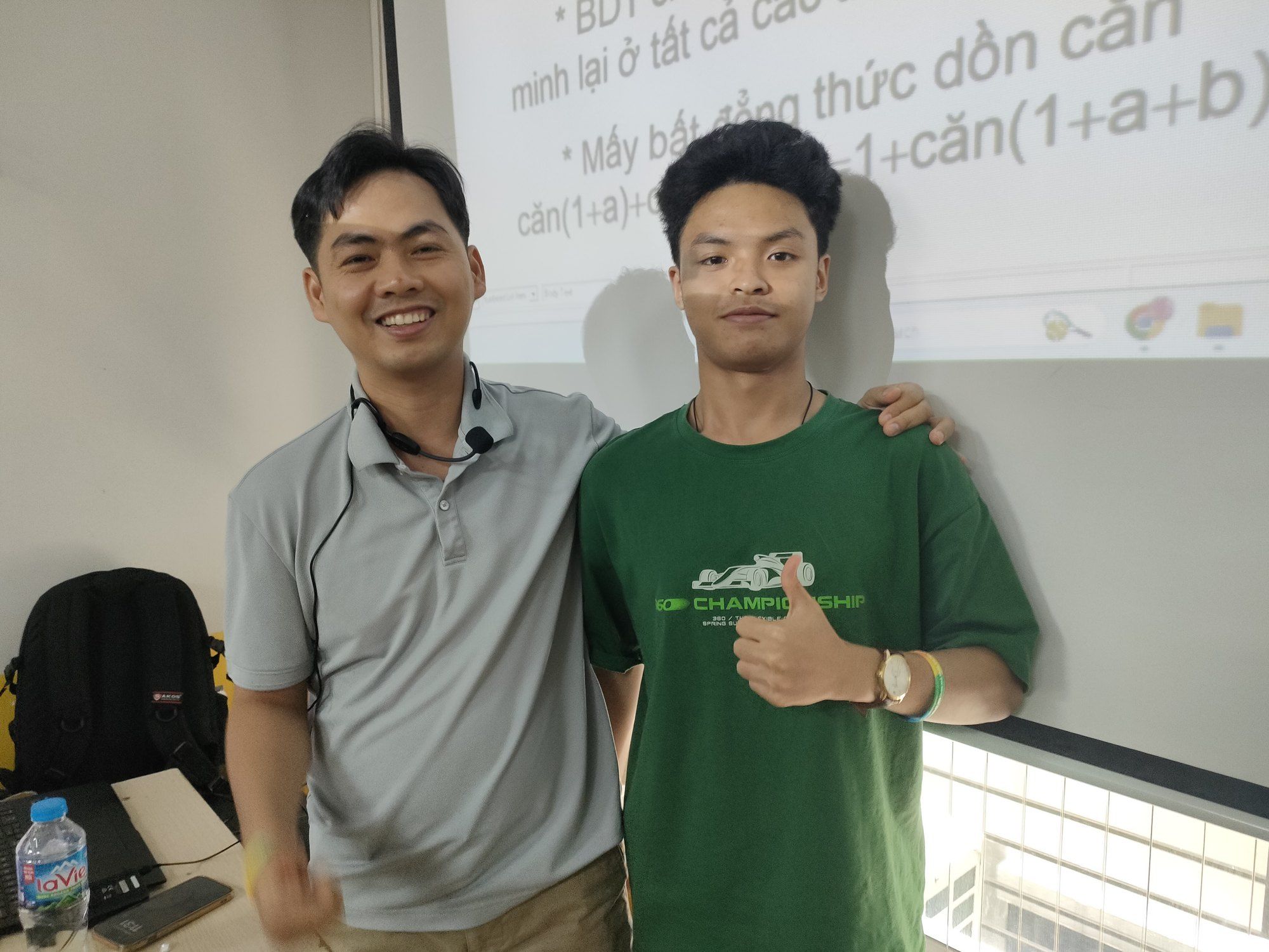Bao with his teacher in a classroom in front of a projected maths lesson.