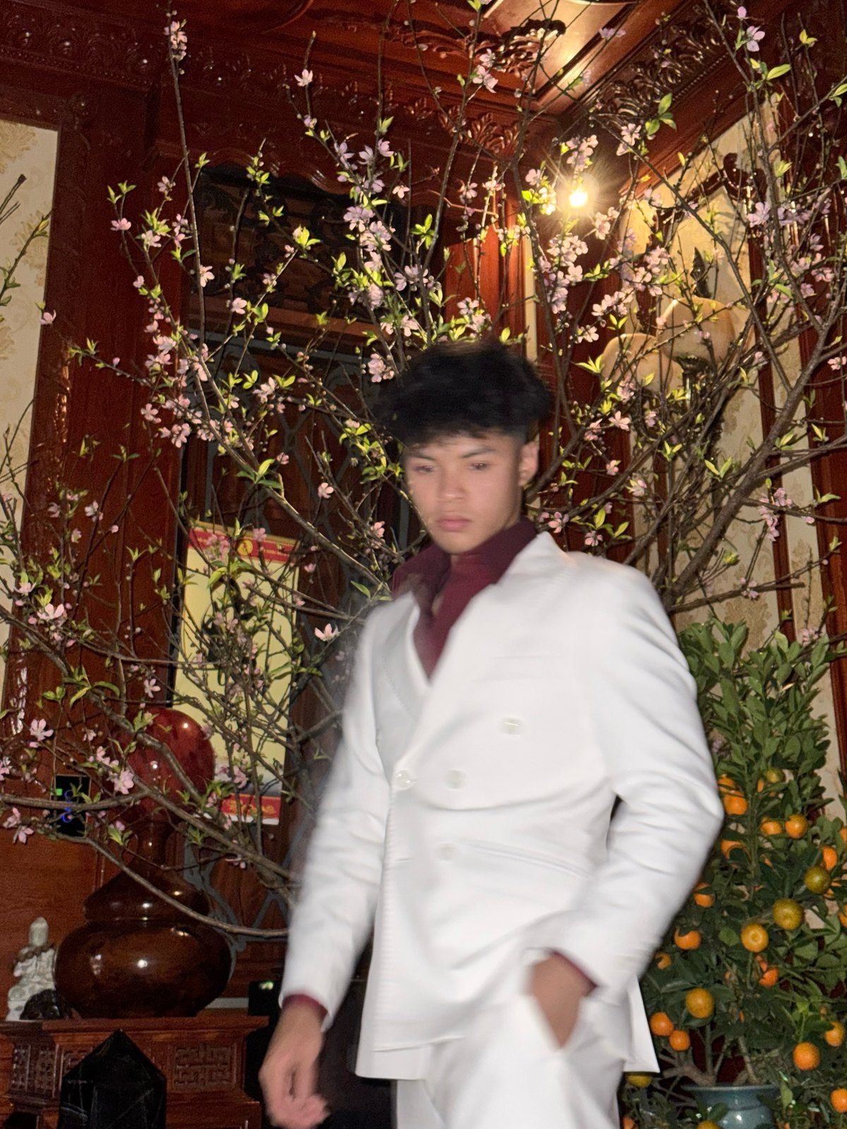 Bao in a white suit beside spring blossoms.
